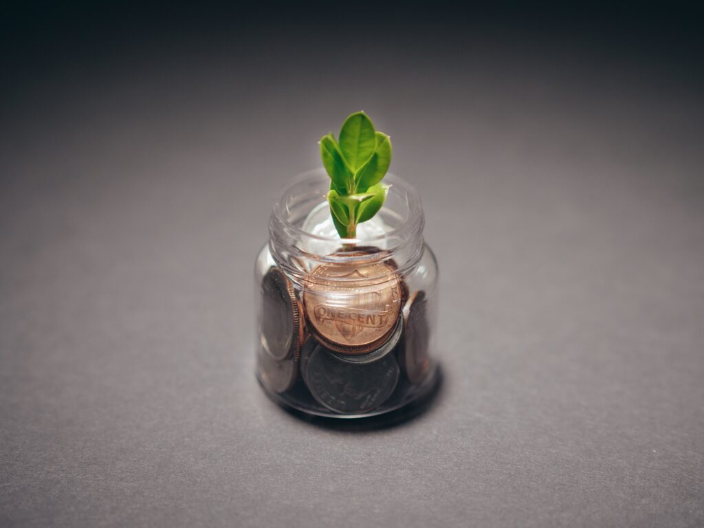 A close up of a small change jar featuring a penny with a plant growing out of it indicating financial growth.
