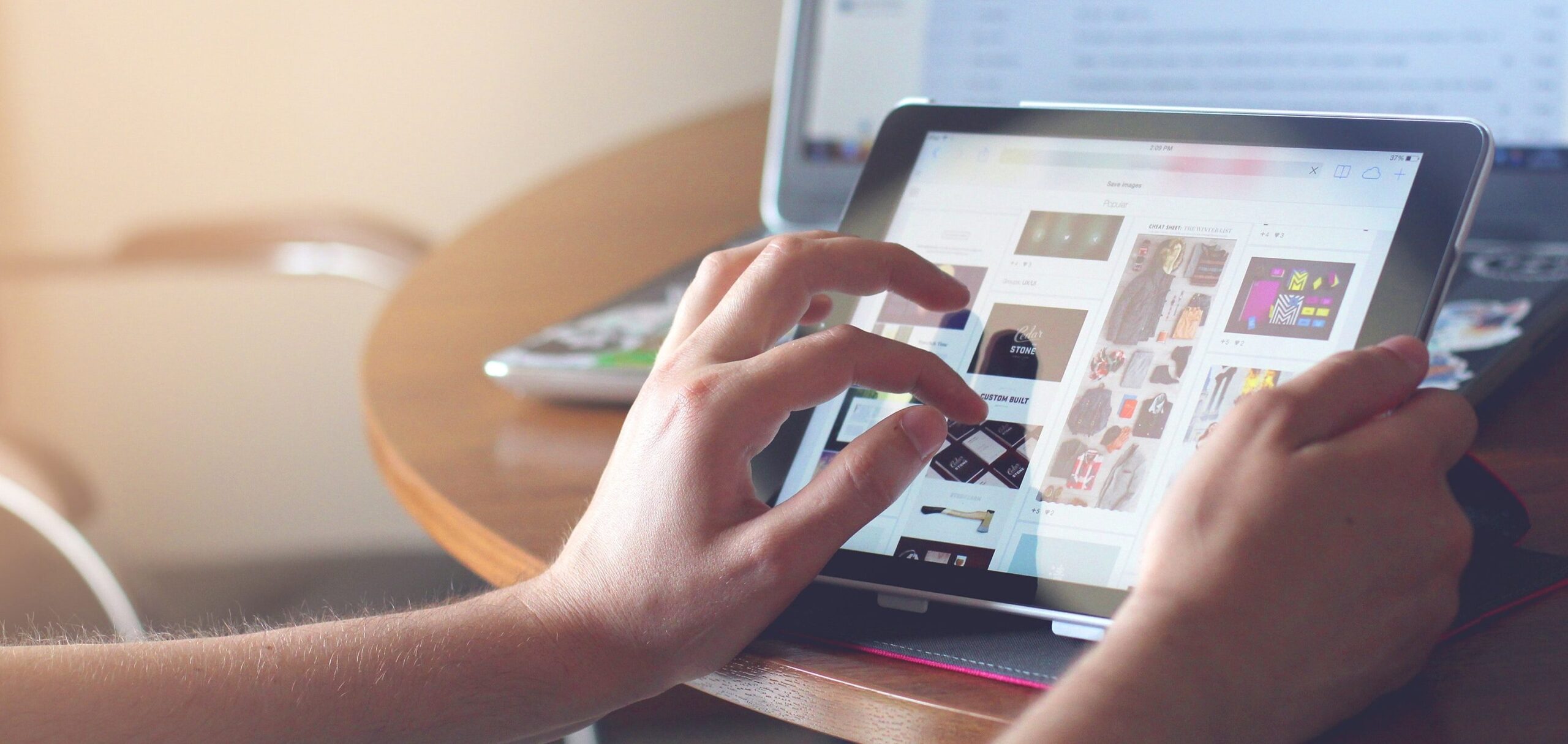 Woman's hand touching a tablet on a table in front of a computer