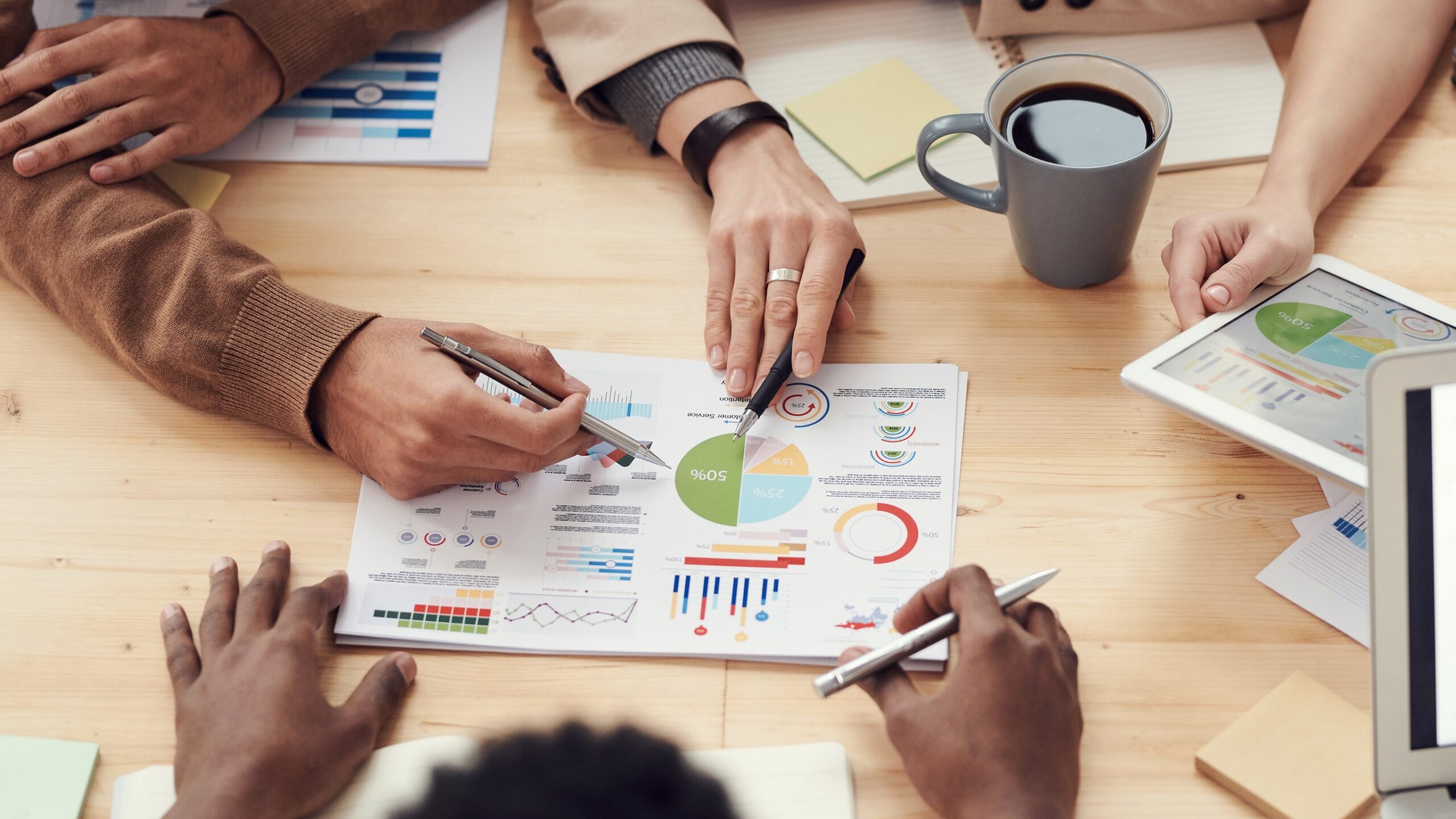 An overhead view of a table top with the visible arms of three people strategizing over colorful charts and graphs