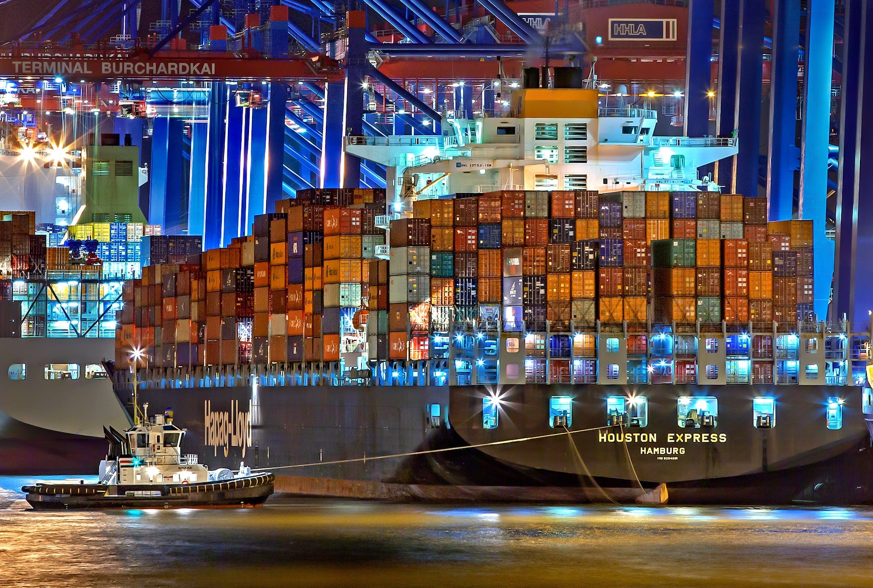 A large container ship in a harbour flanked by a smaller pilot ship