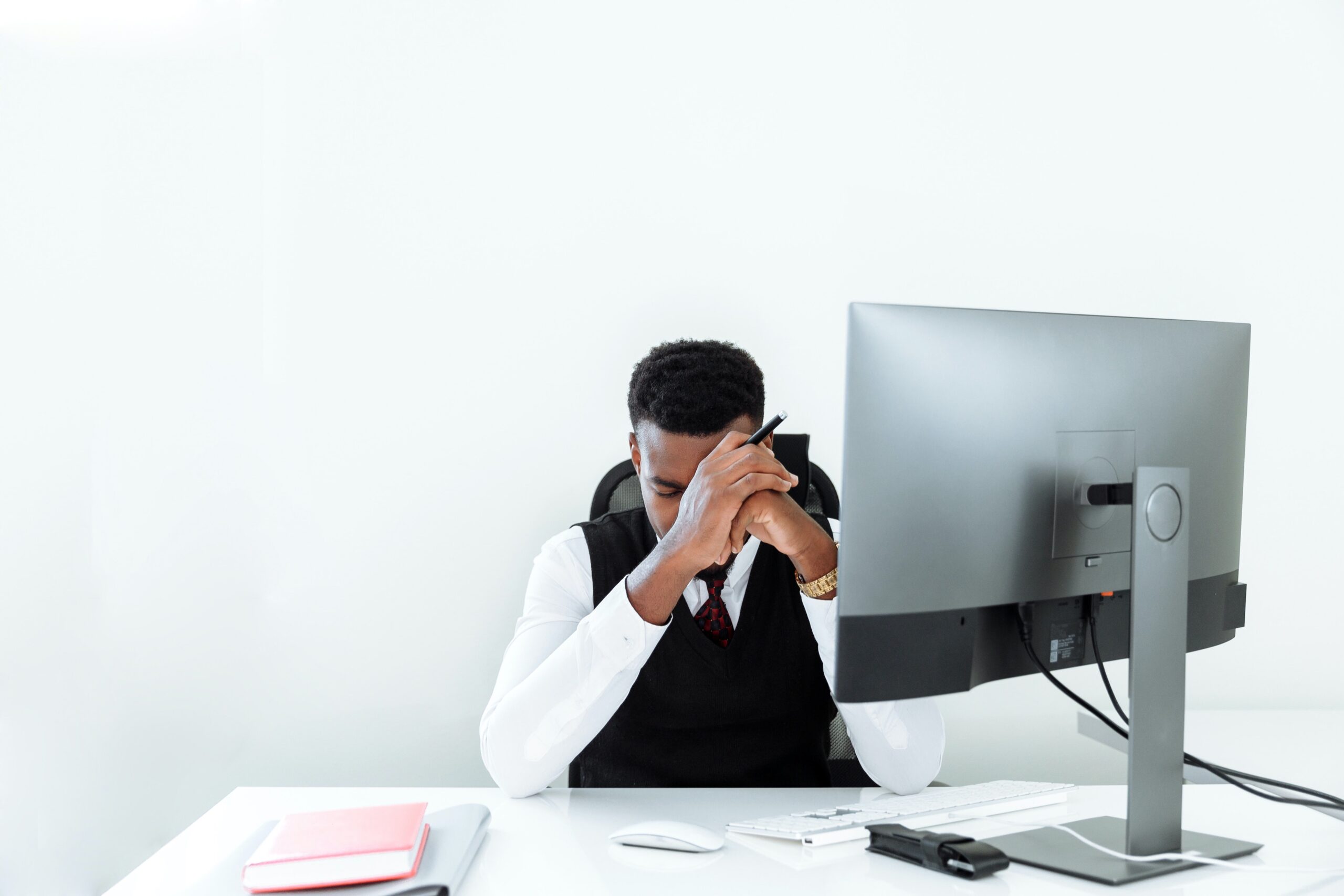 A frustrated man puts his face in his hands in front of his computer at his desk. He appears to have recieved bad news.