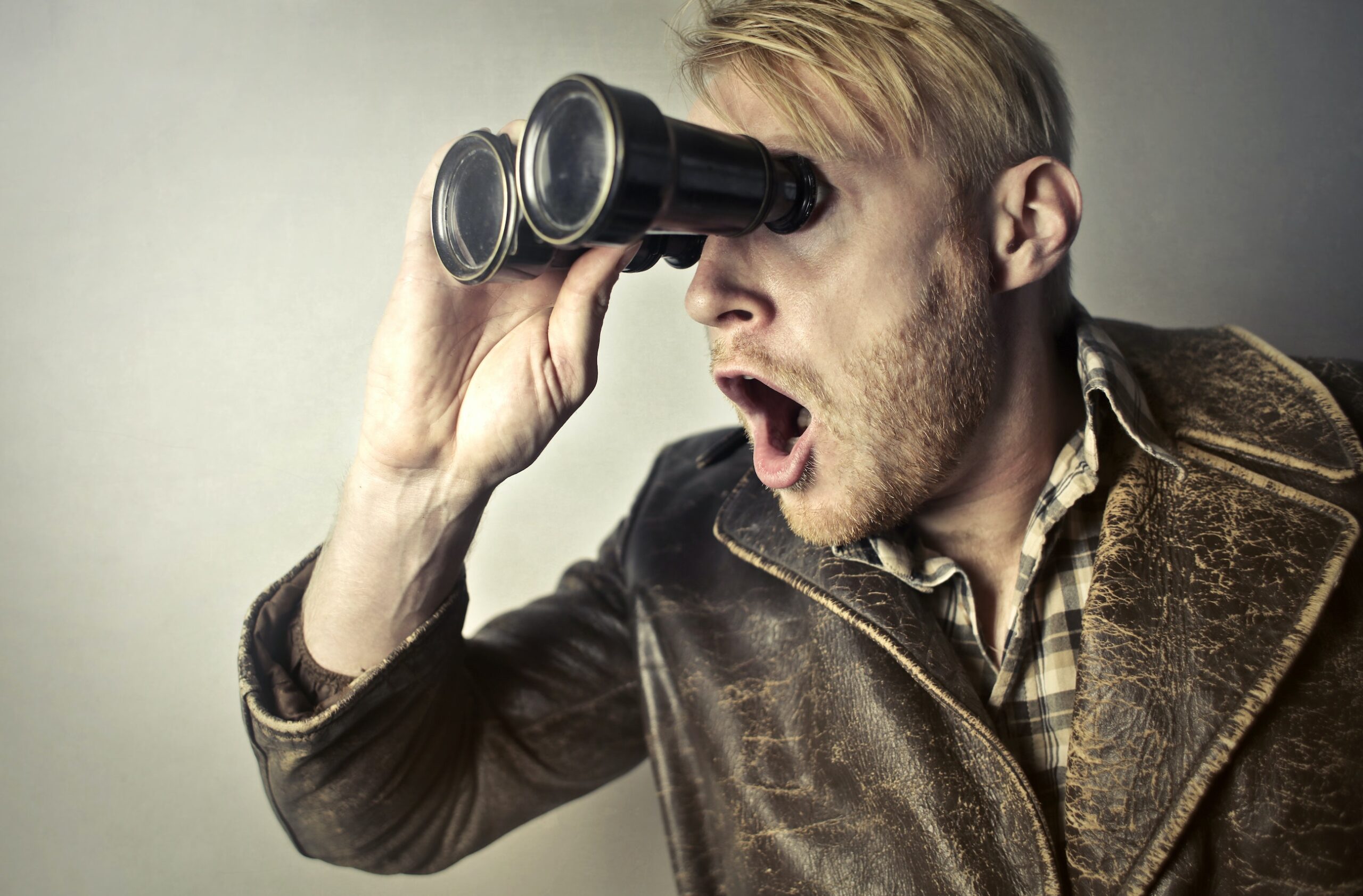 highly emotive man with mouth open looking through binoculars