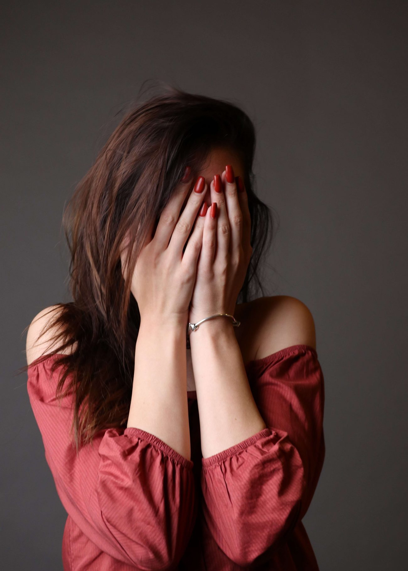 woman with dark hair in red top holding hands over her eyes