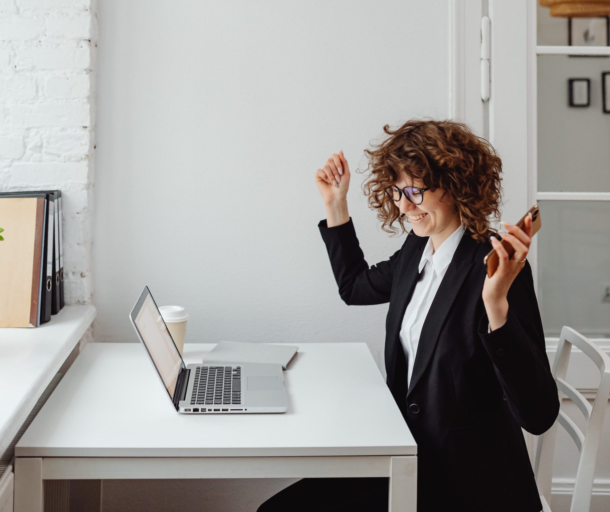 dark haired woman celebrating in front of her laptop