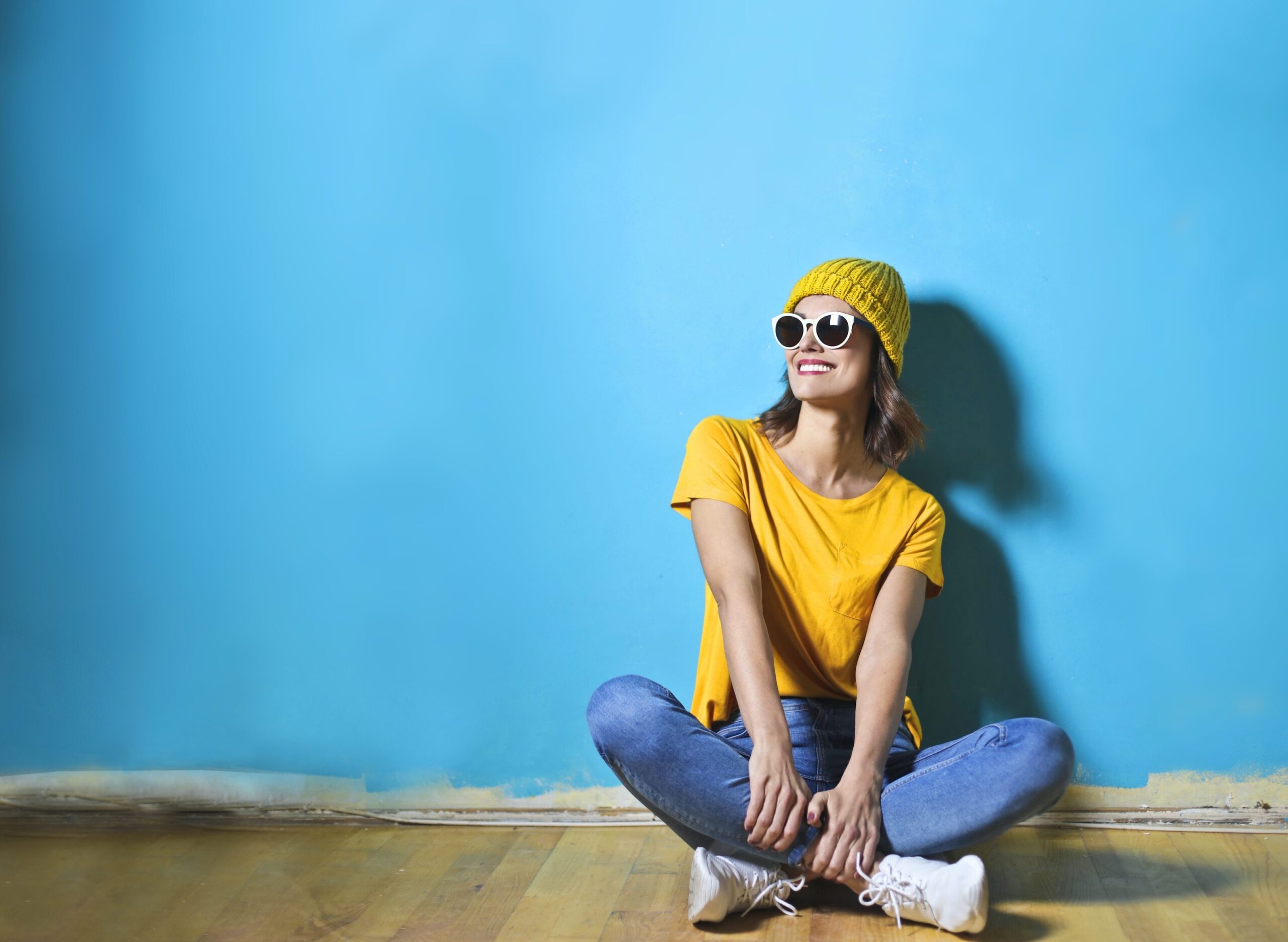 young woman in a ski hat and glasses against a blue wall