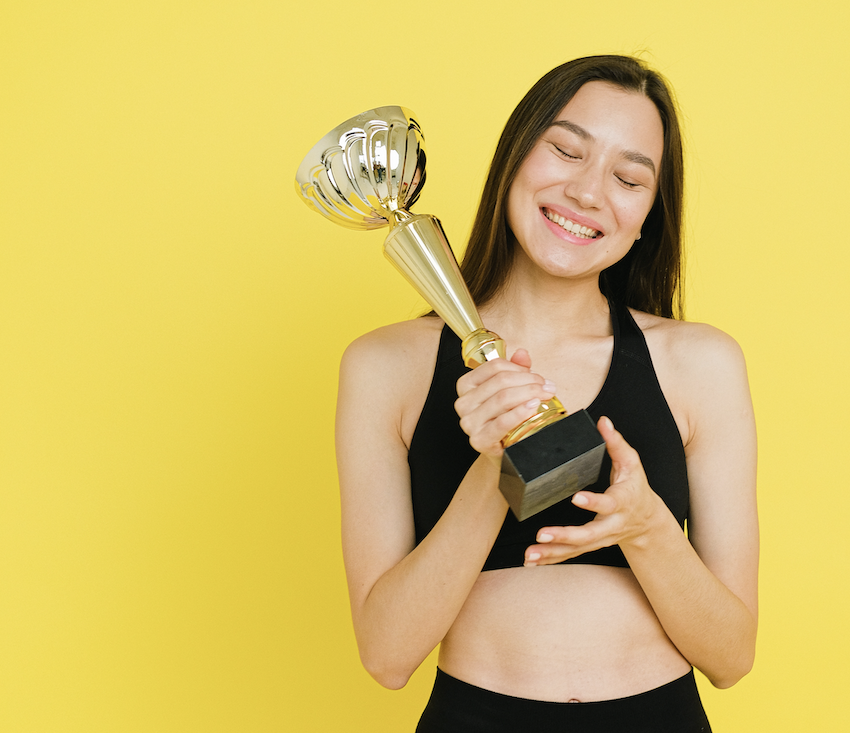 dark haired young woman in a black yoga clothing holding a golden trophy